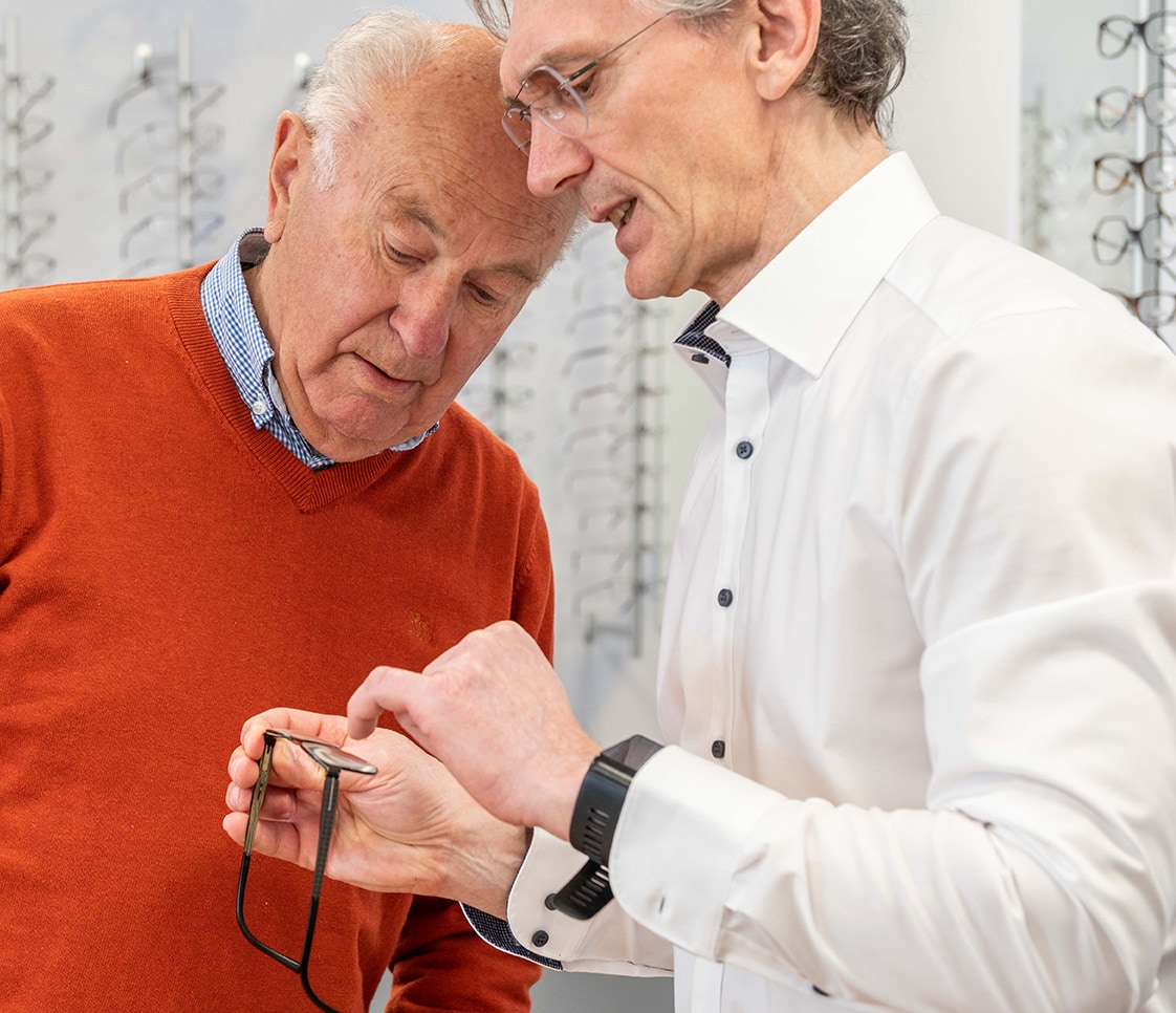 Optiker zeigt Kunden eine Brille und erklärt etwas